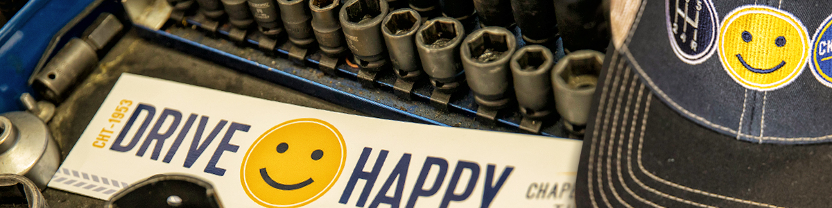 photo of a set of wrenches beside a bumper sticker with a yellow smiley face that reads "Drive Happy" and a blue ball cap with a yellow smiley face