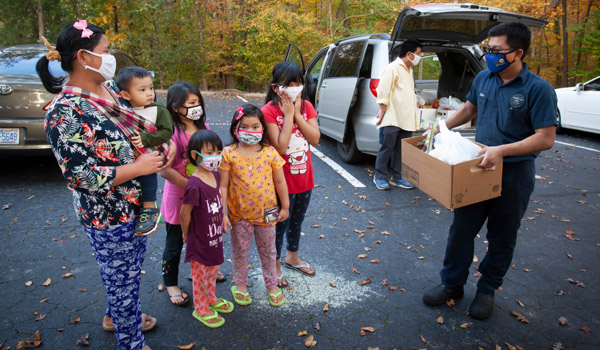 People unload boxes of supplies from a van to share with a family