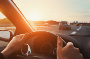 Person holding a steering wheel at sunset