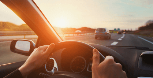 Person holding a steering wheel at sunset