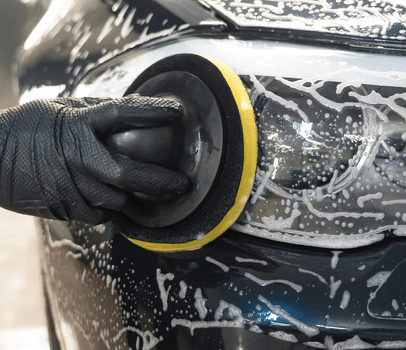Mechanic washes a vehicle's headlights during an advanced car detailing appointment